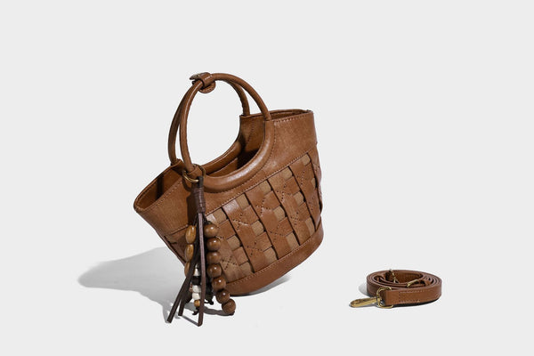 Small woven-panel bucket bag with circular ring handles, beaded tassel charm, and detachable crossbody strap in brown, detail