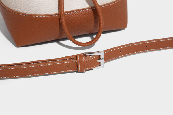 Small two-tone pebbled drawstring bucket bag with tan contrast base, metal toggle hardware, short top handle, and detachable