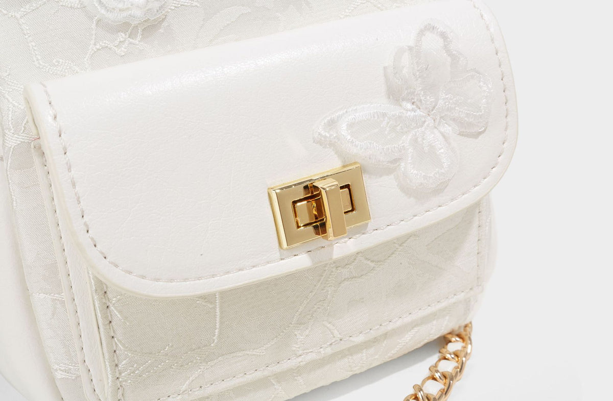 Structured mini backpack handbag with butterfly embroidery, gold-tone chain strap, and turn-lock front flap pocket, detail
