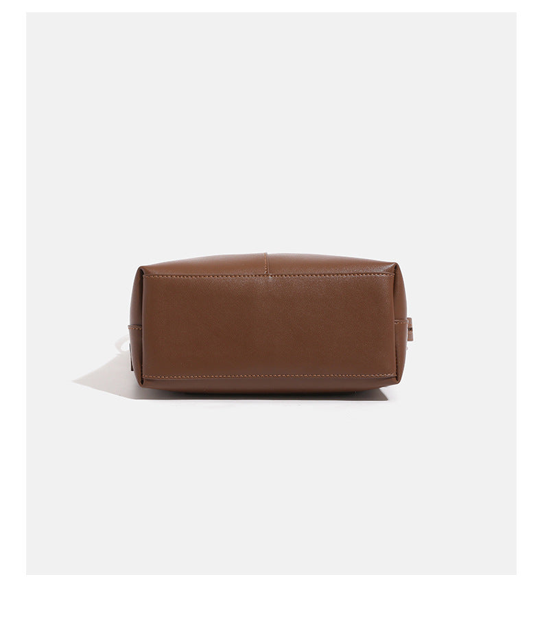 Smooth leather-look bucket bag with long flat shoulder strap, open top, gold-tone hardware, and decorative rabbit charm