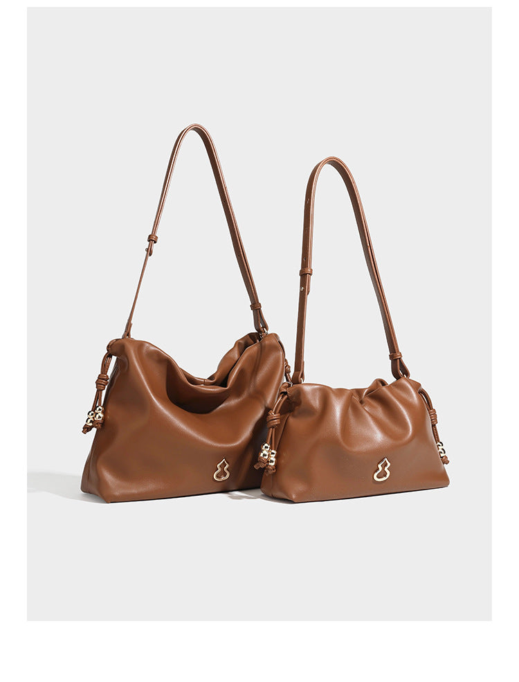 Slouchy ruched drawstring shoulder bag in smooth leather-look finish with gold-tone emblem and slim adjustable strap, detail