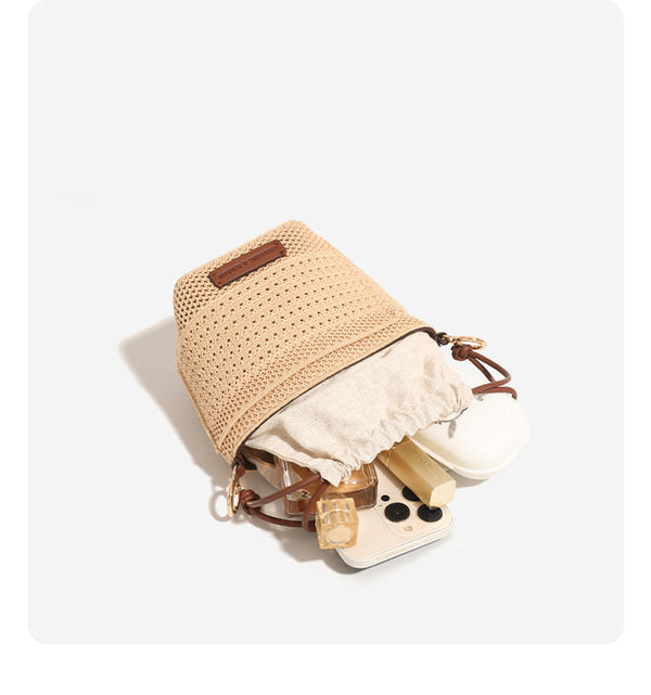 Compact openwork woven bucket bag with gathered cream drawstring liner, leather-look brown trim and cords, and gold-tone
