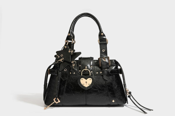 Structured leather-look satchel bag with heart padlock charm, star charm, gold-tone buckle hardware, dual top handles, and