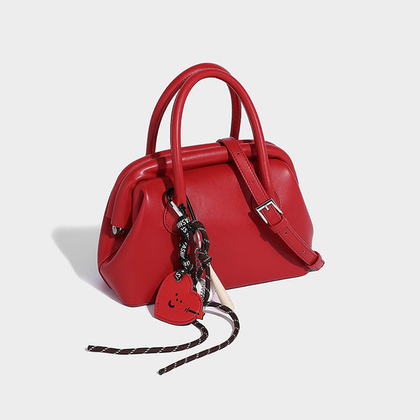 Small structured shell top-handle bag in red with heart charm and braided cord detail, smooth leather-look finish, detail