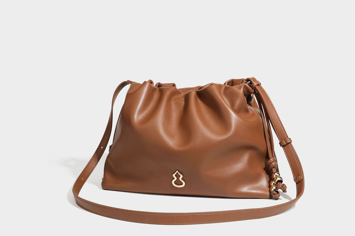 Slouchy ruched drawstring shoulder bag in smooth leather-look finish with gold-tone emblem and slim adjustable strap, detail