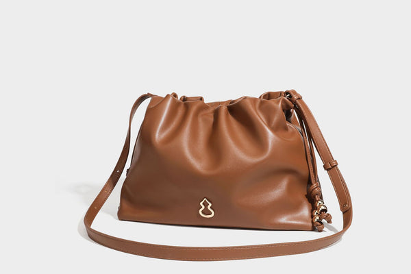 Slouchy ruched drawstring shoulder bag in smooth leather-look finish with gold-tone emblem and slim adjustable strap, detail