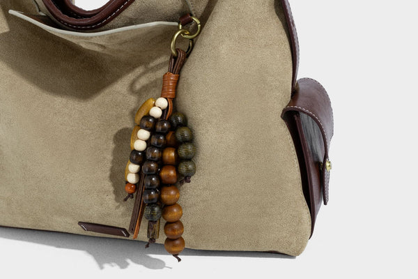 Lässig fallende Hobo-Schultertasche in Khaki aus mattem Material in Wildlederoptik mit dunkelbraunem Besatz in Lederoptik, Quastenanhänger mit Perlen und seitlicher Klappe, Detailansicht