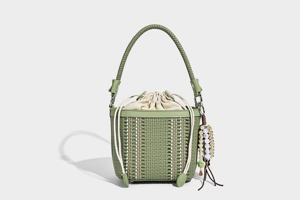 Small woven bucket bag with drawstring top, braided handle, detachable crossbody strap, and silver-tone ring hardware, detail