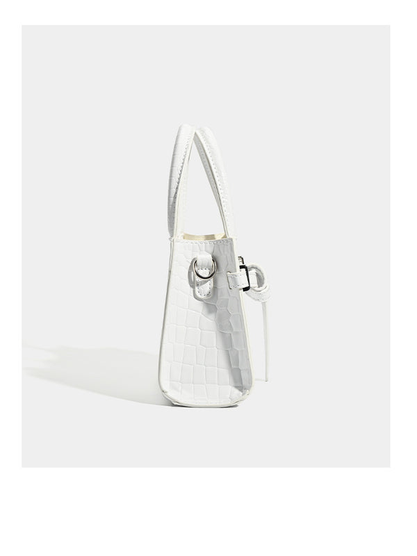 Small structured trapezoid mini top-handle bag with front belt-knot buckle detail and glossy leather-look finish, detail view