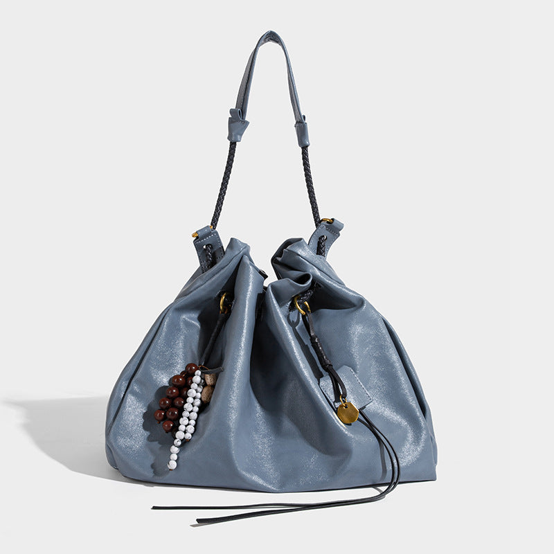 Cream slouchy drawstring bucket bag with braided cord, beaded tassel charm, and gold-tone ring hardware, detail view 2