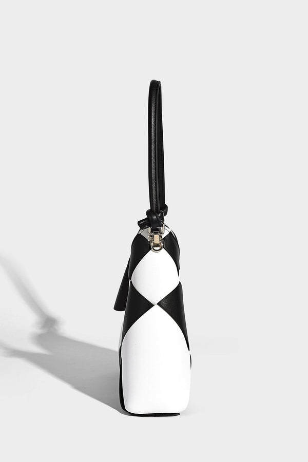 Compact bucket shoulder bag with black-and-white diamond patchwork panels, knotted top handle, gold-tone hardware, and