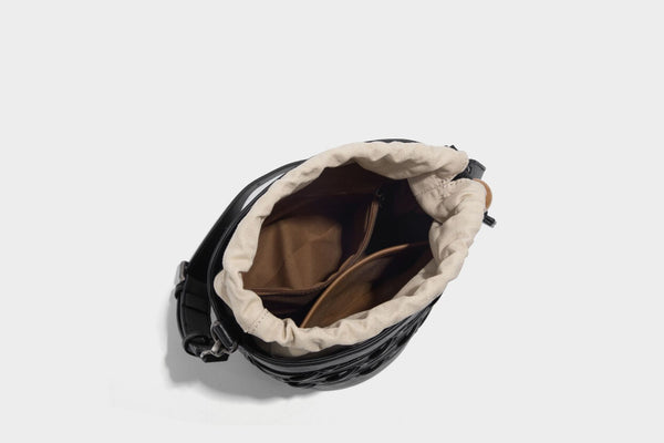 Small cylindrical woven lattice bucket bag with leather-look black trim, beige canvas body, wooden bead drawstring closure