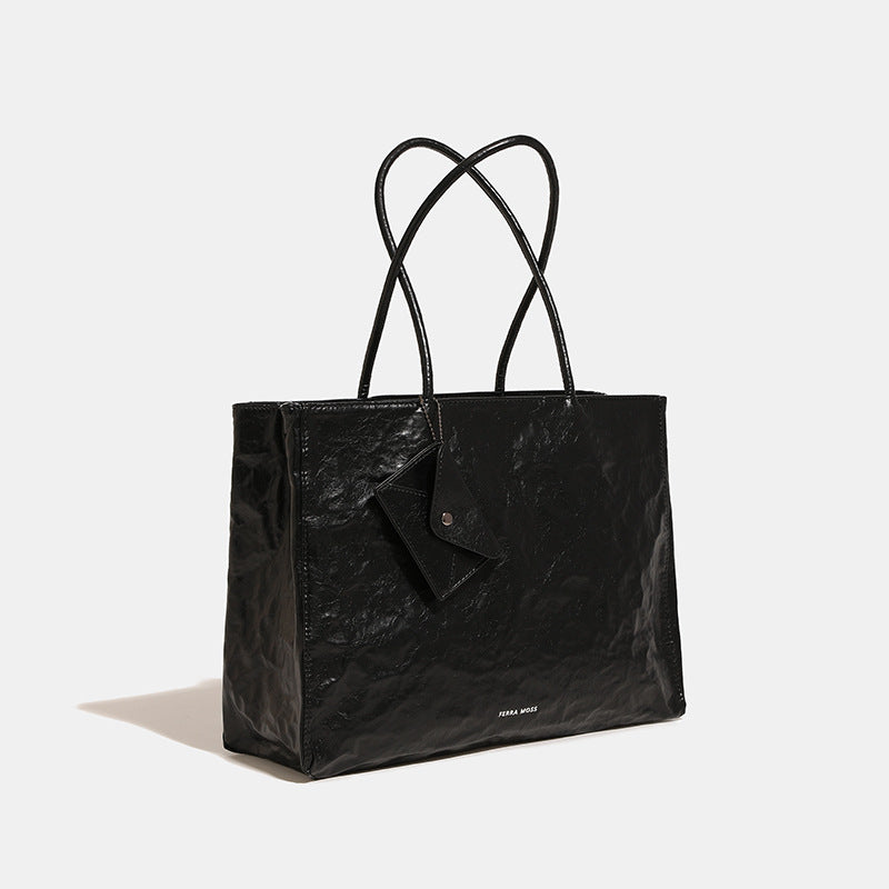 Large glossy crinkled rectangular tote bag with long double handles and hanging envelope snap tag, detail view 3