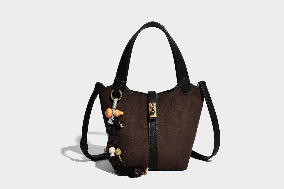 Small structured trapezoid tote bag in matte suede-look finish with black contrast trim, gold-tone front clasp, tassel charm