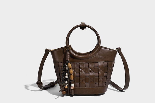 Small woven-panel bucket bag with circular ring handles, beaded tassel charm, and detachable crossbody strap in brown, detail