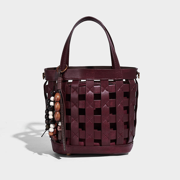 Small woven lattice bucket bag in brown leather-look finish with beaded tassel charm, dual top handles, and detachable