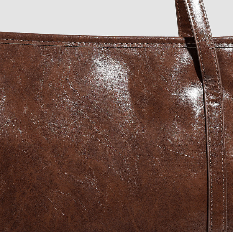 Large structured glossy leather-look tote bag with dual top handles and long shoulder strap in burnished brown, detail view 8