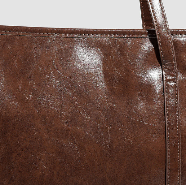 Large structured glossy leather-look tote bag with dual top handles and long shoulder strap in burnished brown, detail view 8