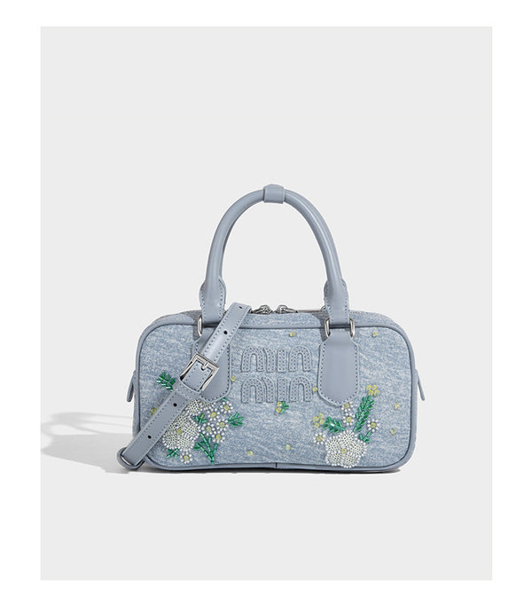 Small light blue denim-look barrel bag with white floral bead embroidery, dual top handles, and detachable shoulder strap