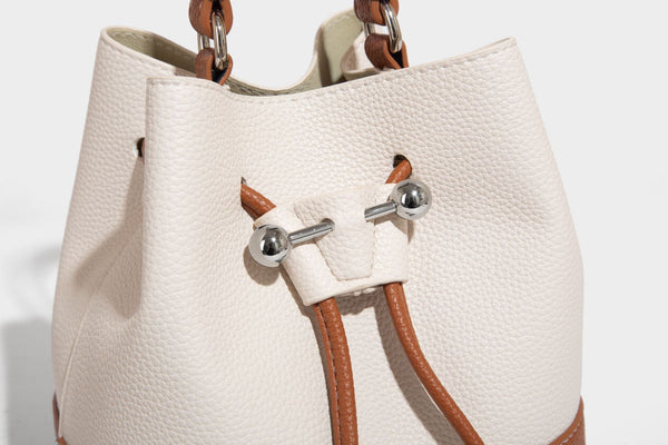 Small two-tone pebbled drawstring bucket bag with tan contrast base, metal toggle hardware, short top handle, and detachable
