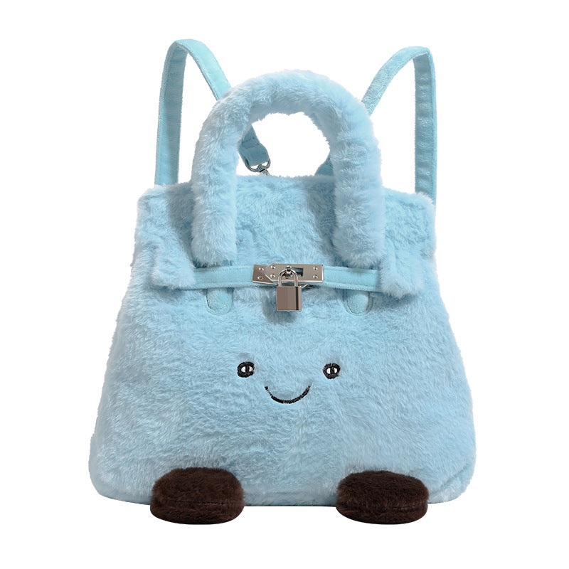 Ice-blue plush faux-fur Kelly-style convertible bag with embroidered smiling face, dark pom-pom feet, silver-tone clasp