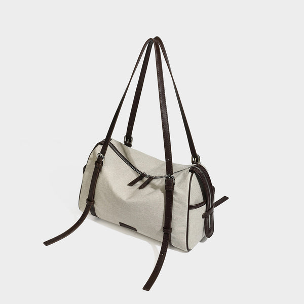Beige canvas barrel bag with dark brown leather-look trim, silver-tone hardware, top zip closure, and adjustable shoulder
