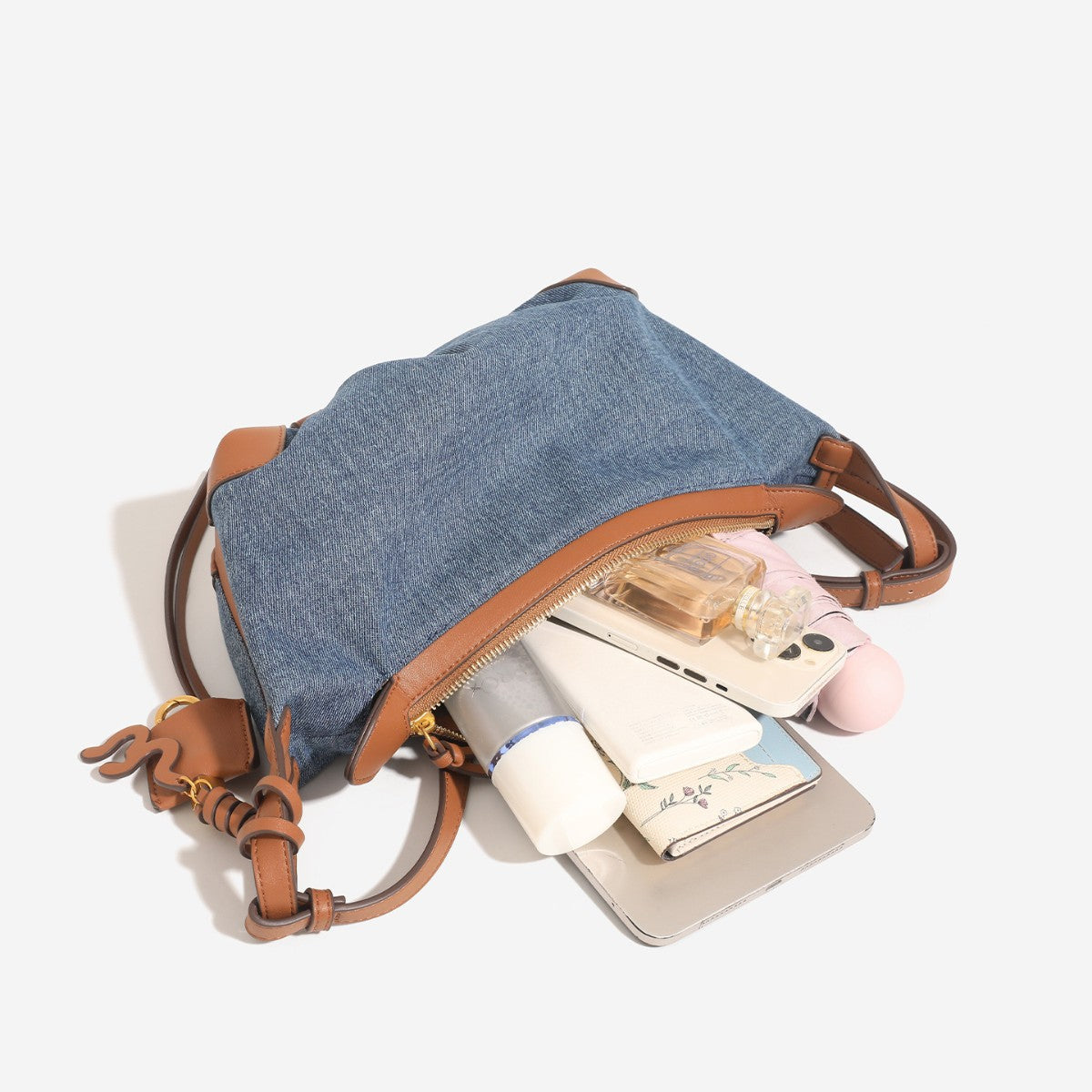 Washed denim canvas crescent hobo bag with tan leather-look trim, knotted strap detail, and gold-tone zipper hardware, detail
