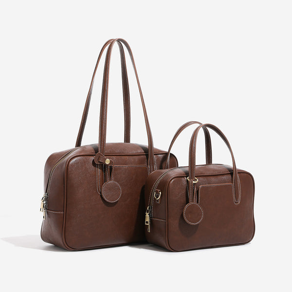 Structured boxy bowling-style tote bag in deep brown leather-look finish with dual top handles, front slip pocket, round