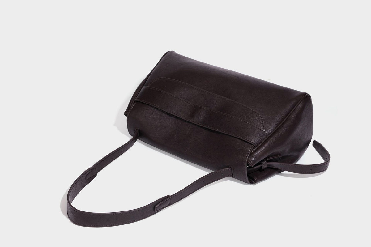 Strukturierte rechteckige dunkelbraune Schultertasche in Lederoptik mit Klappe, mehrlagigem Detail auf der Vorderseite und langem verstellbarem Riemen, Detailansicht