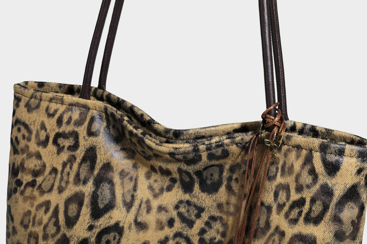 Large leopard print shoulder tote bag in tan and brown with slim dark straps and dangling beaded charm hardware, detail view