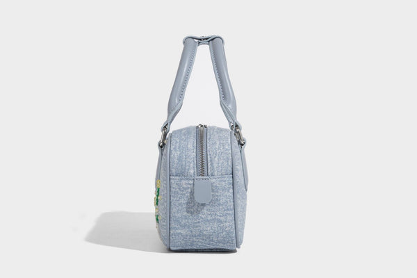 Small light blue denim-look barrel bag with white floral bead embroidery, dual top handles, and detachable shoulder strap