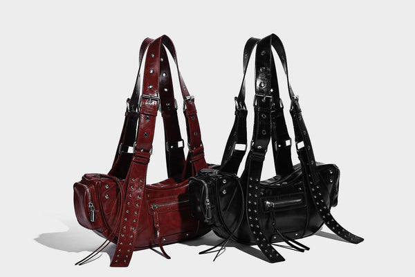 Glossy black crescent shoulder bag with silver-tone rivets, multiple zip pockets, and long adjustable studded straps, detail