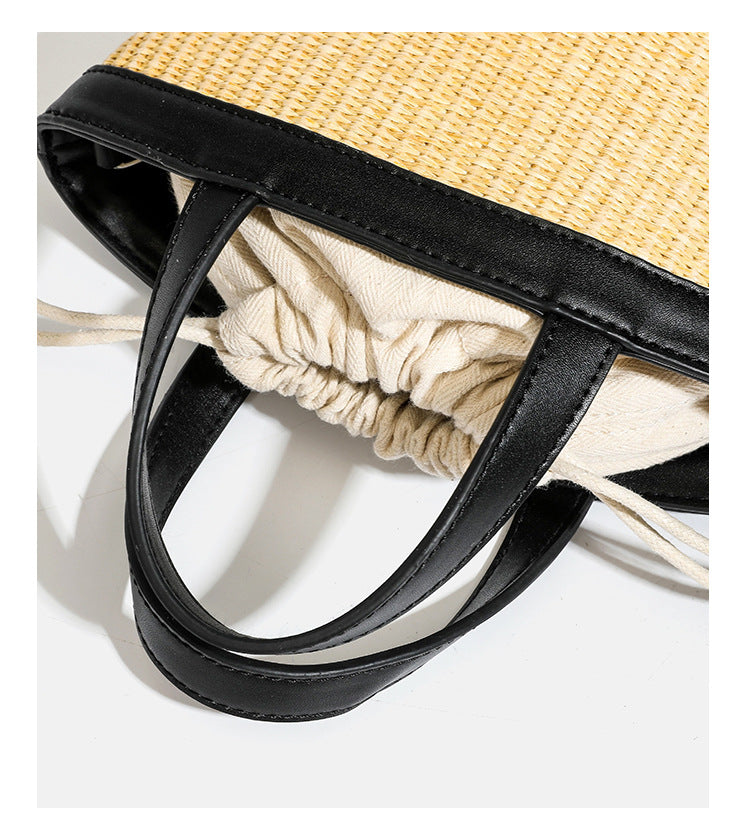Kleine geflochtene Bucket Bag aus Stroh mit schwarzem Besatz in Lederoptik, zwei oberen Tragegriffen, cremefarbenem Futter mit Kordelzug und seitlichen Kordelverschlüssen