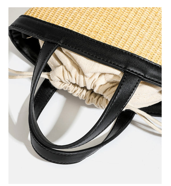 Kleine geflochtene Bucket Bag aus Stroh mit schwarzem Besatz in Lederoptik, zwei oberen Tragegriffen, cremefarbenem Futter mit Kordelzug und seitlichen Kordelverschlüssen