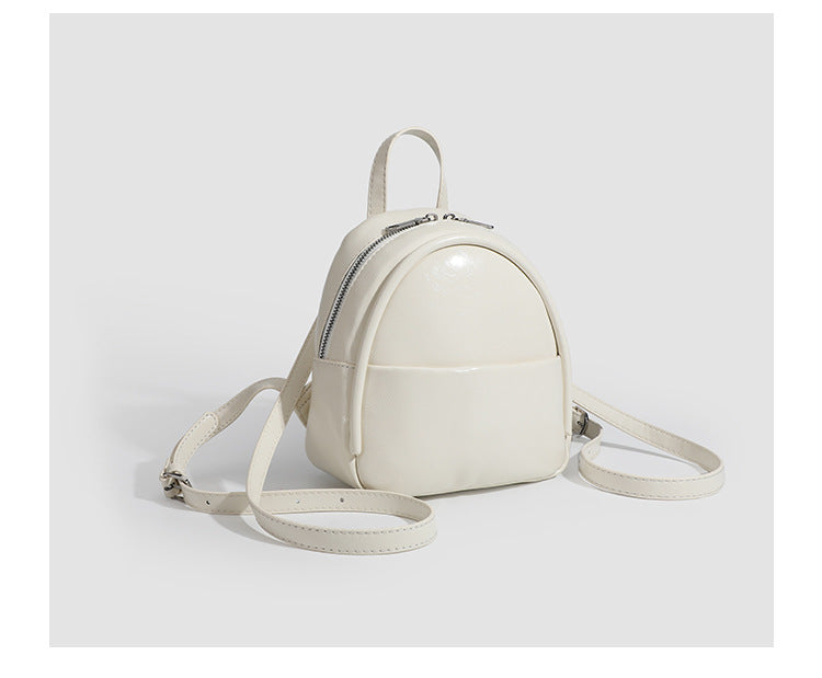 Kompakte, abgerundete Mini-Rucksackhandtasche mit glänzender Lederoptik, Reißverschluss oben, Fronttasche, Tragegriff oben und Detailansicht