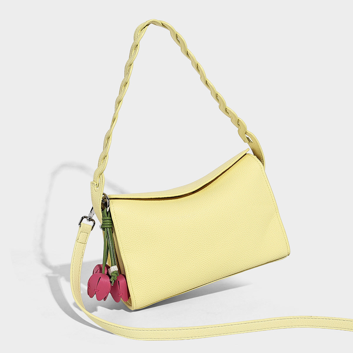 Small structured pebbled-finish shoulder bag with braided top handle, detachable crossbody strap, floral tassel charm, and