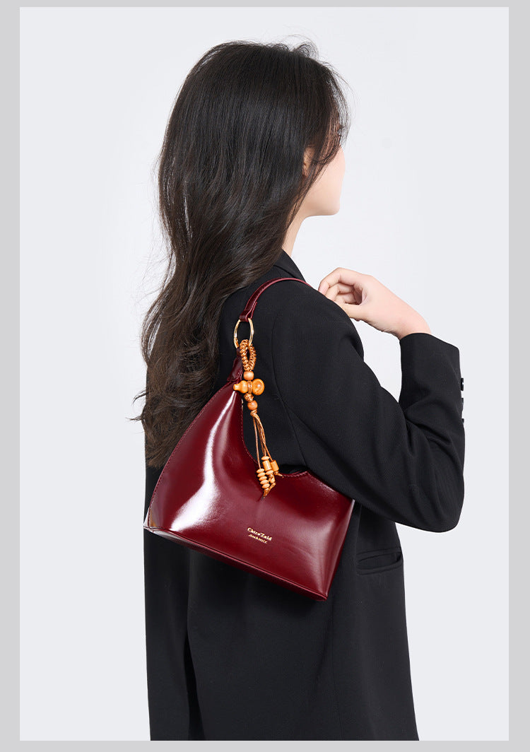 Glossy crescent hobo shoulder bag in deep burgundy with beaded wood tassel charm and gold-tone ring hardware, detail view 9