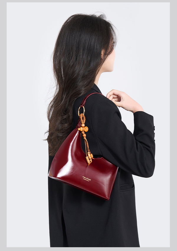 Glossy crescent hobo shoulder bag in deep burgundy with beaded wood tassel charm and gold-tone ring hardware, detail view 9