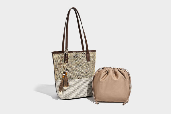Woven straw-look tote bag in tan and cream with dark brown leather-look trim, long flat shoulder straps, and tassel bead