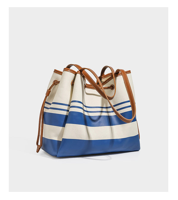 Large cream and navy striped canvas bucket tote bag with tan leather-look trim, drawstring closure, and double shoulder