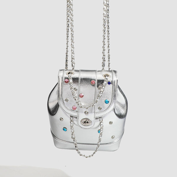 Kompakte silberfarbene Metallic-Rucksacktasche mit mehrfarbigen Kristallnieten, rundem Klappverschluss mit Drehverschluss und ineinander verflochtenem Silber