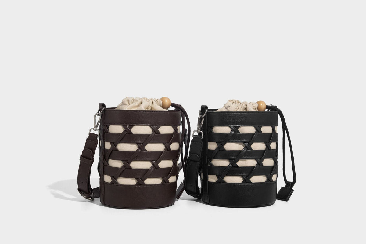 Small cylindrical woven lattice bucket bag with leather-look black trim, beige canvas body, wooden bead drawstring closure