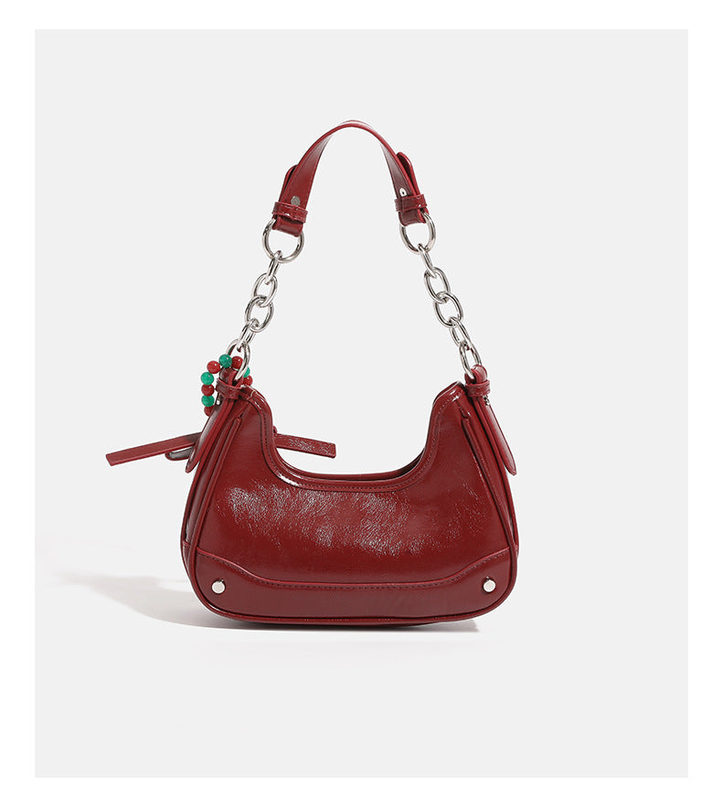 Small glossy cherry red crescent shoulder bag with silver chain strap, bead and tassel charm, and round pendant, detail view