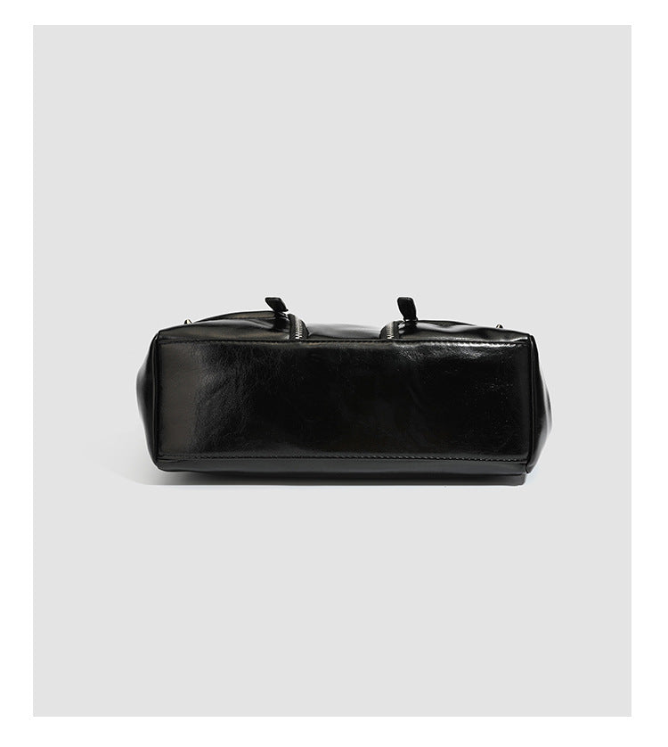 Black glossy structured tote bag with rivet and buckle detail, dual top handles, and detachable shoulder strap, detail view