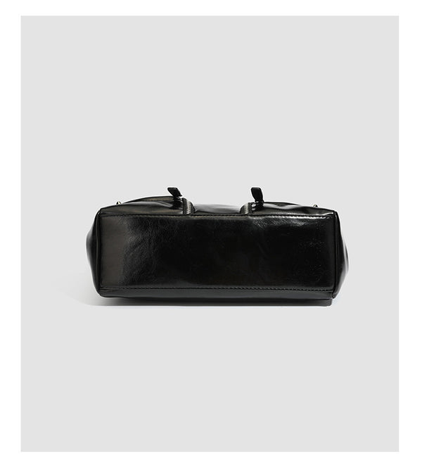Black glossy structured tote bag with rivet and buckle detail, dual top handles, and detachable shoulder strap, detail view