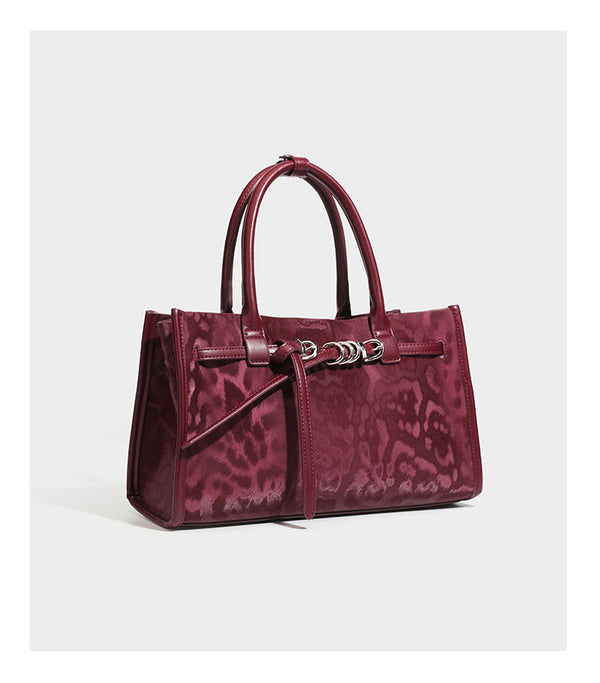 Structured leopard-print tote bag with glossy satin-like finish, dual rounded top handles, silver buckle-and-ring front