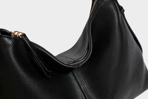 Slouchy hobo shoulder bag with pebbled leather-look finish, zip-top closure, gold-tone hardware, and hanging bead charm