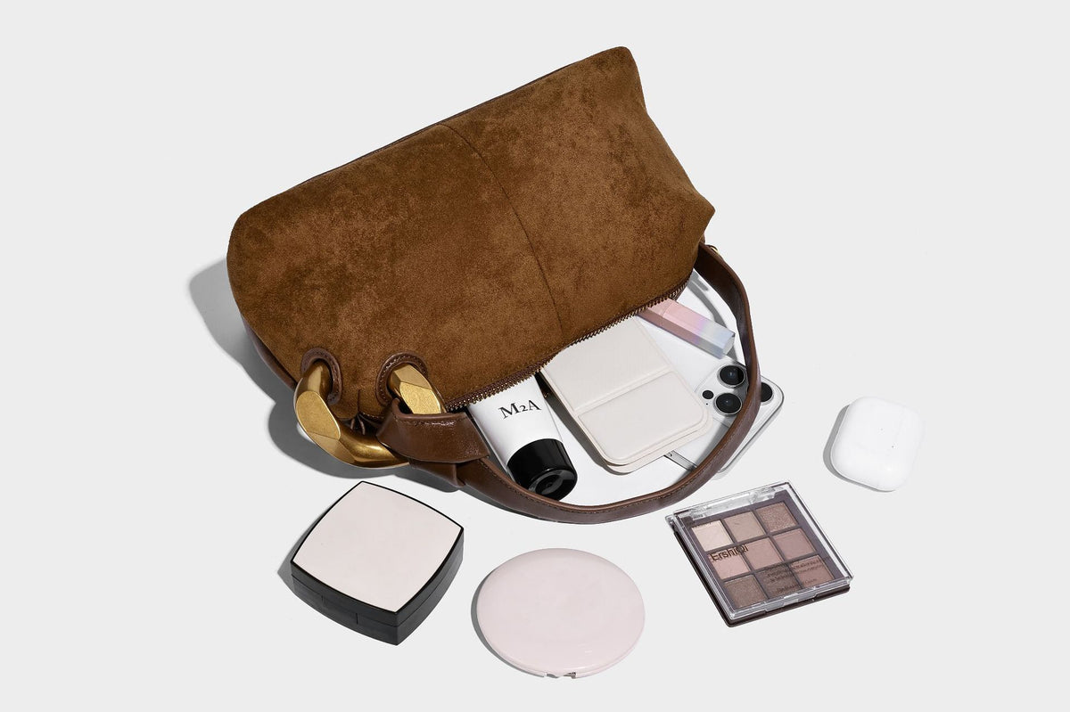 Kompakte Boston-Schultertasche in warmem Braun in Wildlederoptik mit glattem dunkelbraunem Besatz, übergroßen goldfarbenen Ringelementen und Reißverschluss oben