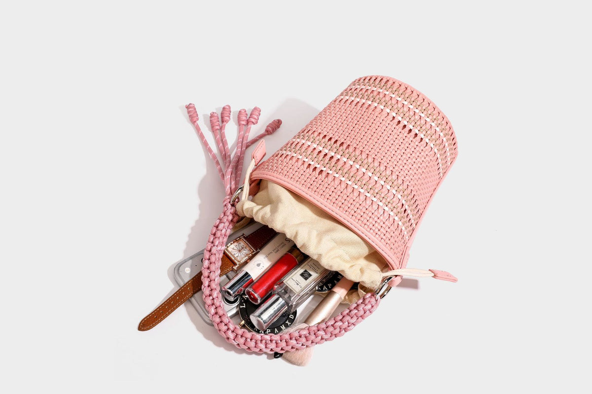 Detailansicht einer zylindrischen, handgeflochtenen Beuteltasche mit geflochtenem Henkel, Kordelzugverschluss, Kordelquasten und Metallringbeschlägen