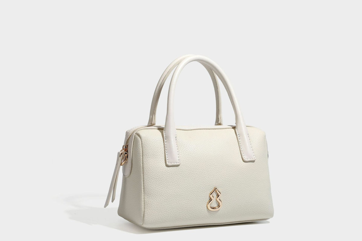 Small structured pillow satchel bag with pebbled leather-look finish, dual rolled top handles, gold-tone gourd emblem, and